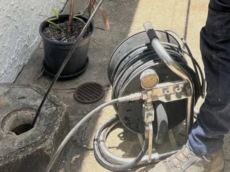 A drain jetting reel and hose running into an open drain beside a house