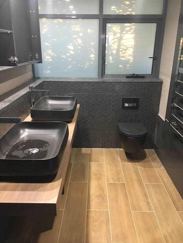 A bathroom with two black basins on a timber bench and a wall-hung black toilet