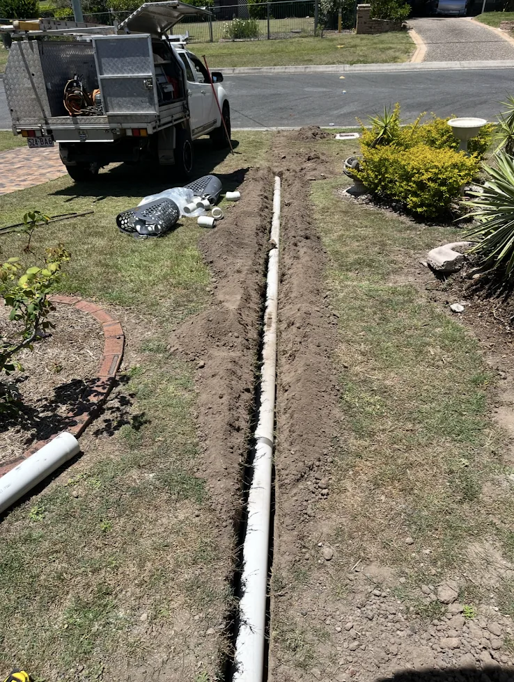 A new white drain pipe laid in a long trench across a front lawn