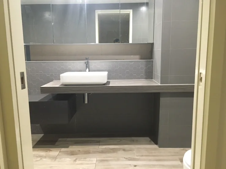 A floating stone vanity with a white basin under an LED mirror