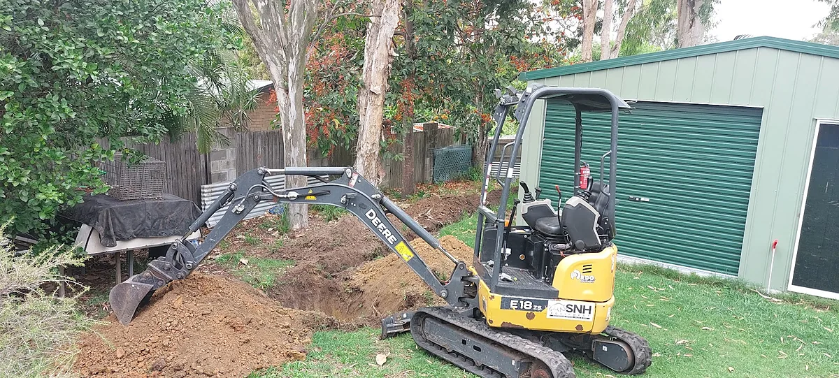 A mini excavator trenching for new stormwater pipes in a backyard