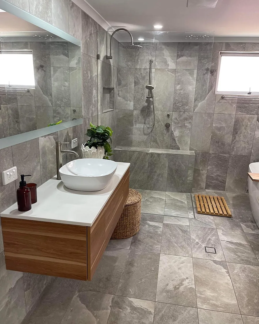 A grey stone-look tiled bathroom with a walk-in shower, rain head and timber vanity